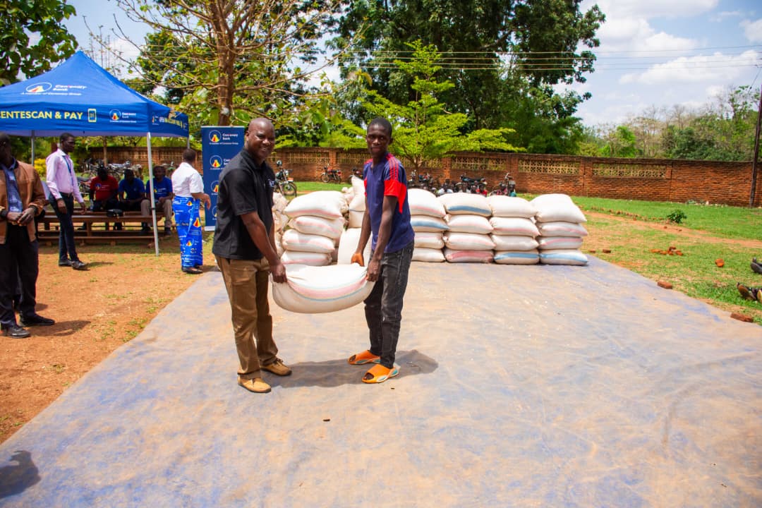 Fr. Mangwere, Centenary Bank chaplain helps lift a bag of one of the beneficiaries